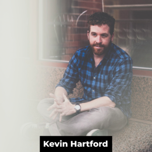 A white man with brown hair and beard wearing a blue plaid shirt, watch, and grey jeans sits cross-legged in front of a wall. At the bottom of the photo are the words 'Kevin Hartford' in white bold text on a black rectangle.