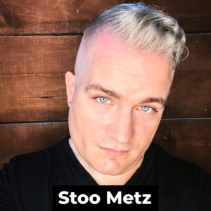 A white non-binary person with silver hair and blue eyes wearing a black shirt looks at the camera. At the bottom of the image in white text on a black rectangle are the words ' Stoo Metz'.